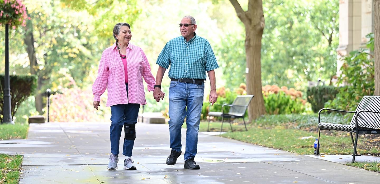 An older couple walks hand-in-hand on 51ƷƵ's campus