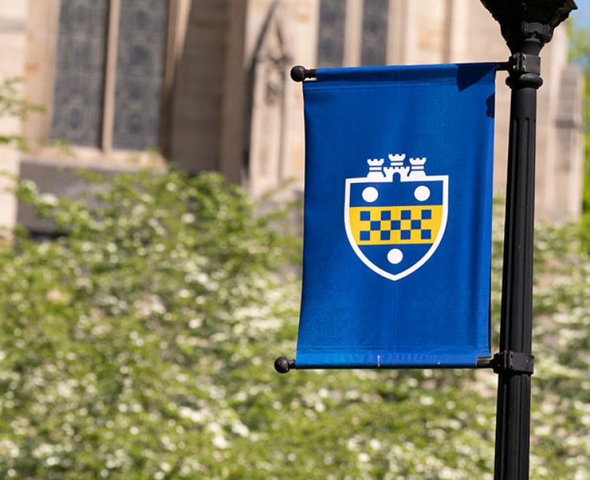 A blue flag with a 51ƷƵ shield in front of the Cathedral of Learning